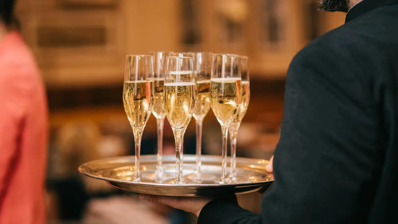 Kelner trzyma srebrną tacę z kieliszkami szampana podczas eleganckiego przyjęcia